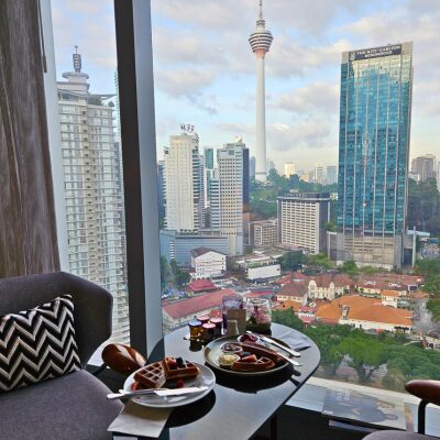 クアラルンプールの街並みとKLタワーを背景に、窓辺で並べられたルームサービスの朝食セット。
