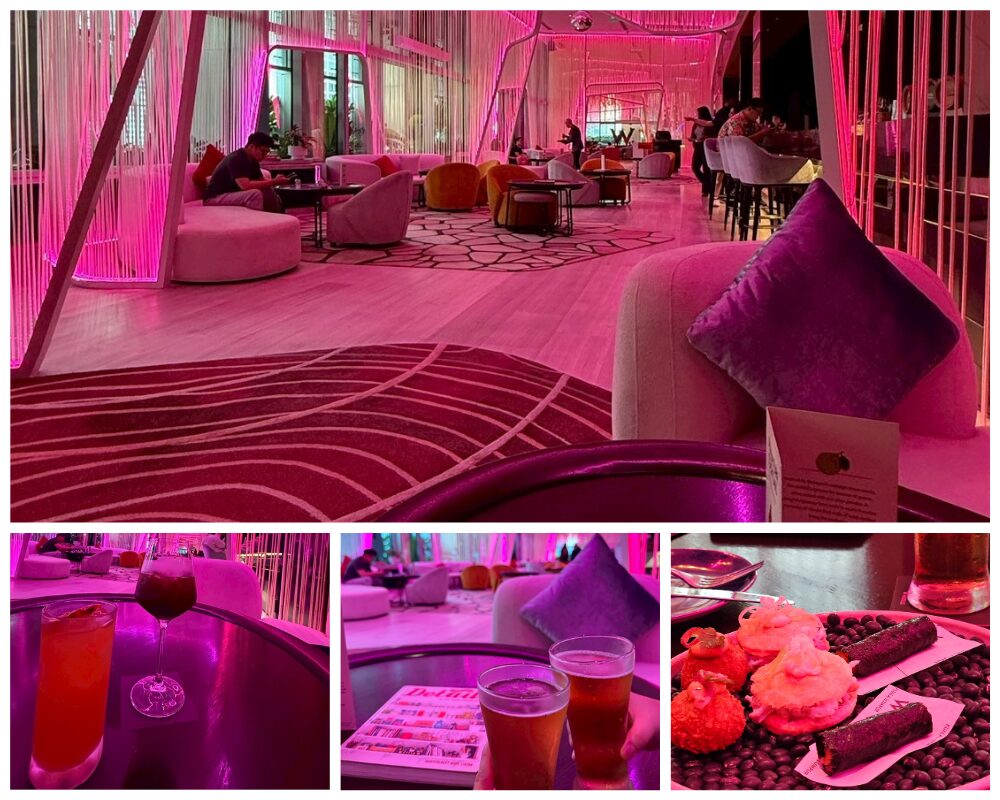 Wクアラルンプールのバーで提供されるハッピーアワーの様子。ピンク色のライトに包まれたラウンジ、カクテル2杯、ビールと雑誌のテーブル、そして軽食プレートが並ぶ席の雰囲気を撮影した写真。