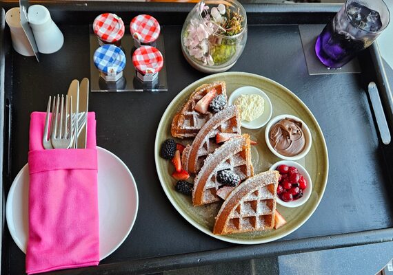 ワッフルとベリーの朝食プレートが並んだルームサービスのトレー。色とりどりのジャムやクリームが添えられている。